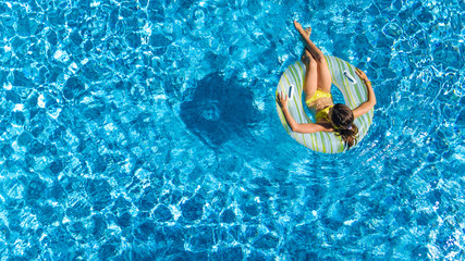 Aerial top view of girl in swimming pool from above, kid swims on inflatable ring donut , child has fun in water on family vacation
