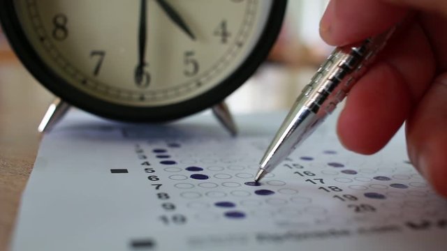 Students taking exams writing on optical form of standardized exam near Alarm clock with holding yellow pen for final examination in secondary school, college university classroom, Education concept