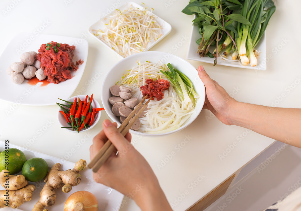 Wall mural female chef prepare traditional vietnamese soup pho bo with herbs, meat, rice noodles