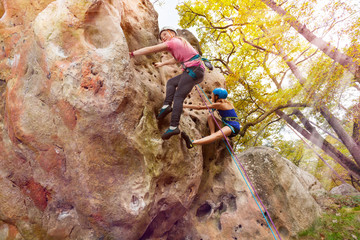 Alpinists climbs a rock with harnesses in woodland