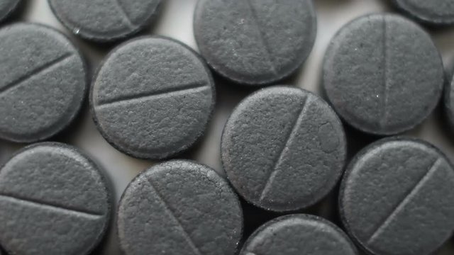 Many activated coal tablets rotating, on white background