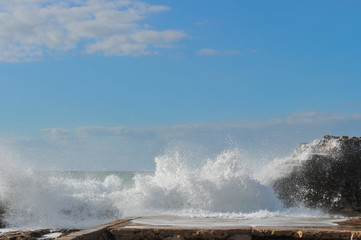 Waves breaking over coastal cliffs and breakwater during the storm, making a big splash of seawater