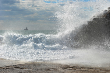 Waves breaking over coastal cliffs and breakwater during the storm, making a big splash of seawater