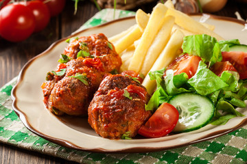 Roasted meatballs in tomato sauce with french fries and salad