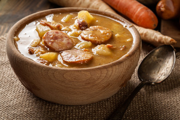 Wooden bowl of split pea soup with sausage and potatoes