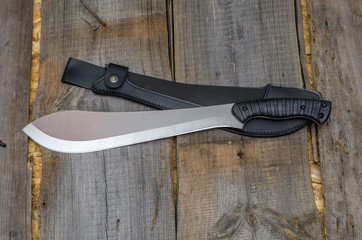 Obraz premium A machete with a leather case on a wooden background. Working knife.