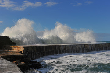 Waves breaking over coastal cliffs and breakwater during the storm, making a big splash of seawater