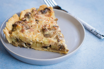 Slice of tart with mushrooms, potato and cheese on gray plate on table background. Copy space