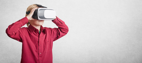 Horizontal shot of small boy wears VR glasses, sees virtual reality, isolated over white background with copy space for advertising content. Male child in virtual headset glasses. Future, progress