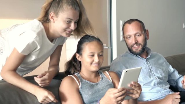 Father with his daughters talking and using tablet on sofa at home
