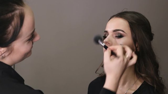 make-up artist applies powder with a professional brush on the face of the girl