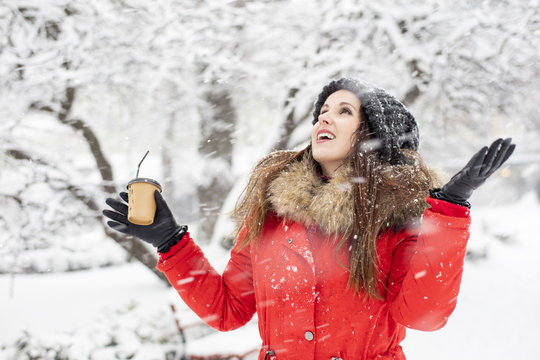 a girl in red winter coat with fur and cup of coffe apploudsing on the street in winter day