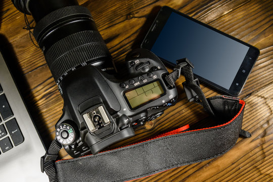 Modern DSLR camera, smartphone and laptop on wooden table. Top view