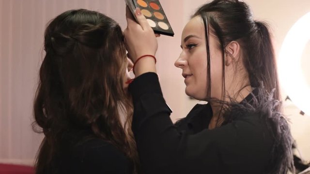 make-up artist applies shadows with a professional brush and communicates with the model