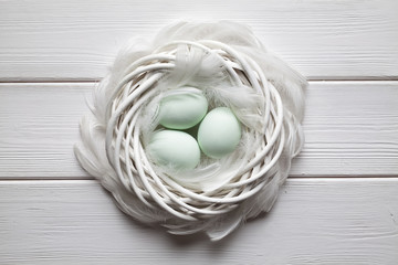 Three easter eggs and feathers in the nest on wooden table