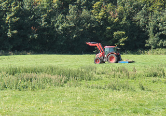 An Agricultural Farm Tractor Cutting the Grass in a Field.