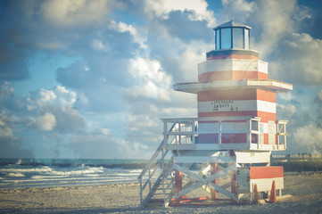 Bright scenic view of an iconic red and white striped lifeguard tower with puffy white clouds in...