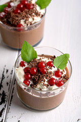 Chocolate mousse with currant and mint in a glasses on a whiite wooden background.