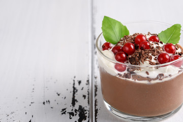 Chocolate mousse with currant and mint in a glasses on a whiite wooden background.