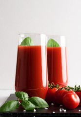 Tomato juice in a glass with a cherry and basil on a light background