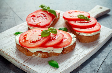 Bruschetta, toast with soft cheese, basil and tomatoes on a white wooden board. Italian healthy snack, food.