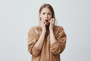 Emotional pretty female with blonde hair stares at camera with dark eyes, looks with bated breath,...
