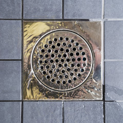 Metal drain hole in the tiled floor of a shower
