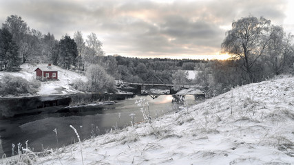 Winter landscape. red cottage next to river.