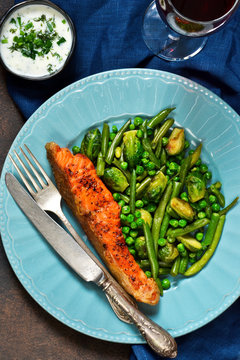 Baked salmon steak with asparagus, Brussels sprouts and green peas on a concrete background with a glass of wine.