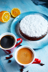 whole biscuit sprinkled with powdered sugar on the blue plate and two red cups of coffee, cut lemon and badon on blue wooden background