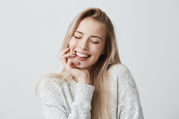 Beautiful female closing eyes because of joy, with long blonde hair and gentle smile. Cheerful...