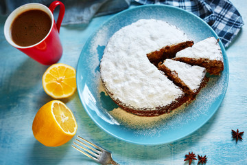 cut biscuit sprinkled with powdered sugar on the blue plate and red cup of coffee, cut lemon and badon on blue wooden background