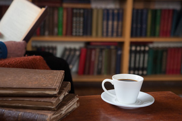 Naklejka premium Sweet moments of relaxation with books and a cup of coffee. Vintage books, glasses, chair, library, man