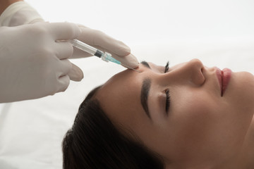 Close up of surgeon hand injecting botox into female forehead. Asian woman closed eyes with serenity