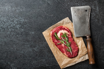 Raw rib eye steak and butcher knife on blackboard