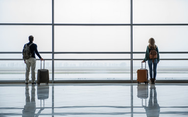 Unacquainted man and woman standing with bags in different parts of the airport hall