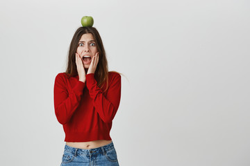 Young emotional caucasian woman with long dark hair looking at camera with popped eyes, screaming in terror, keeping her hands in cheeks, exclaiming. Scared and terrified girl dressed casually