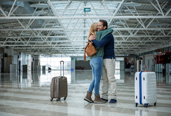 Two cheerful adults hugging each other before departure while standing in the terminal. Suitcases...