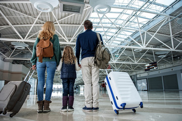 Low angle of man and woman holding hands of their little girl. Their baggage is beside them