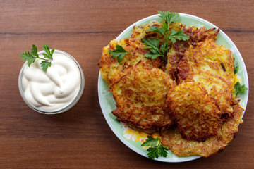 Homemade fried potato pancakes with sour cream on wooden table