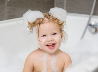 Happy little cute girl bathes in a bath with foam and soap bubbles and  laughing
