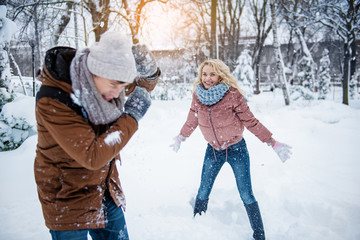 Excited blond girl is throwing snow on her friend. She is standing in forest and laughing
