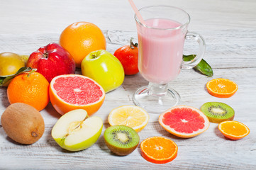 Milk, fruit cocktail in a glass and a fruit mix on a light, wooden background.