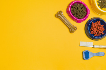 Dry dog food in bowl and pet accessories on yellow background top view. Pet feeding concept backgrounds with copy space. Frame composition.