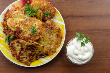 Homemade fried potato pancakes with sour cream on wooden table