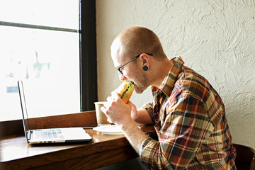 Smiling bearded businessman wearing casual hipster clothing using laptop and cell smartphone in coffe house.