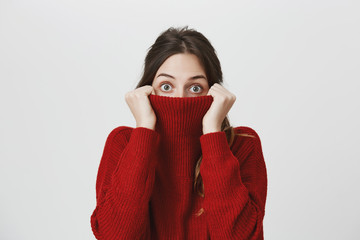 Fashionable cute girl with brown hair hiding in her warm winter sweater, isolated over white background. It was bad idea to watch horror movie alone at night. She will call her friend to come over.