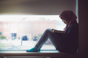 A muslim teenager from Asia reading a book in an apartment in Niagara Canada