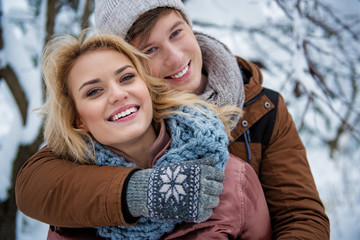 Fototapeta premium Waist up portrait of carefree young man and woman embracing and smiling. They are standing in winter forest and looking at camera with happiness