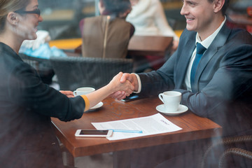 Outgoing female shaking hands with happy colleague. They sitting at table in cafe. Job concept